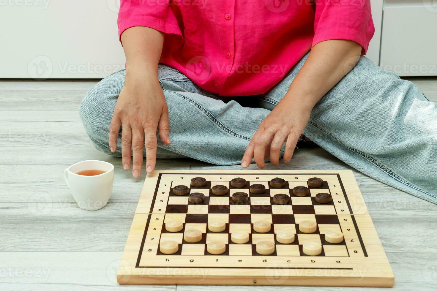 woman in jeans and a crimson shirt with a cup of tea playing chess at home photo