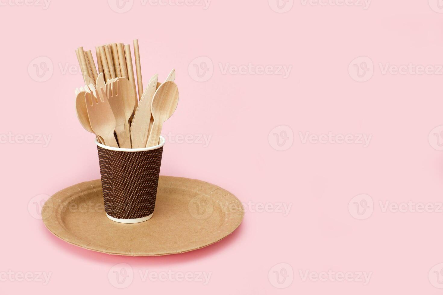 disposable bamboo cutlery in a paper cup on a paper plate on a pink background with copy space photo