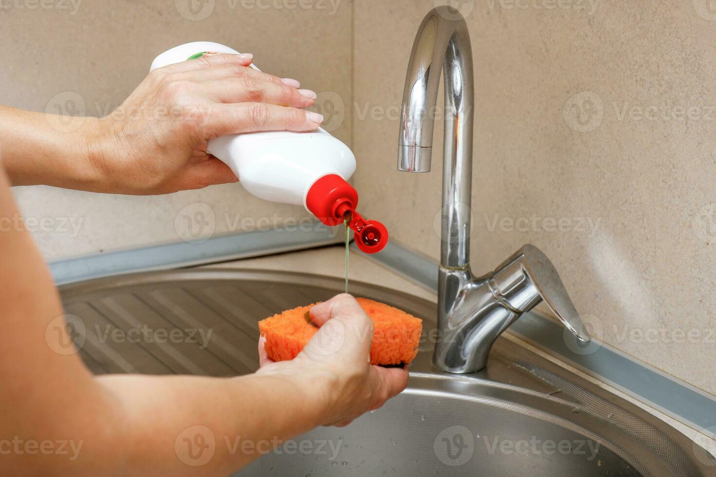 woman's hands pour detergent on a sponge over a sink with a water tap photo