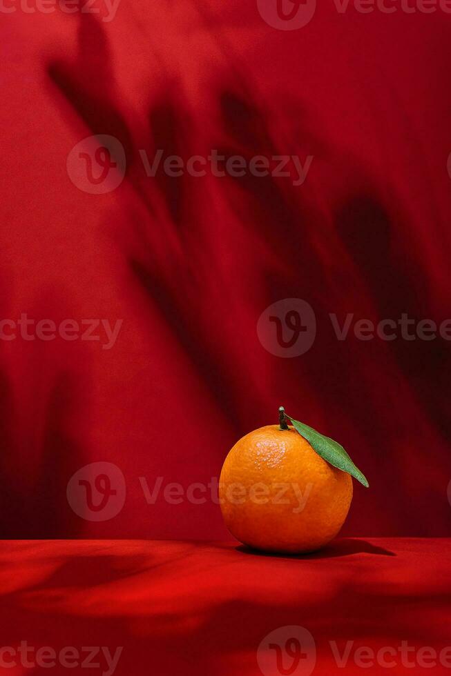 Ripe tangerine with green leaf on red background photo