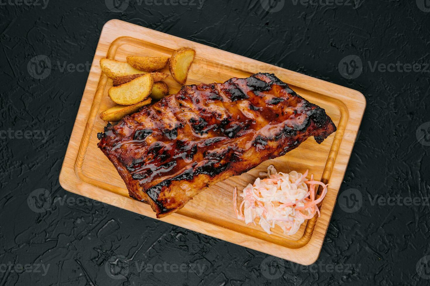 Pork loin ribs served on chopping board and potato wedges photo