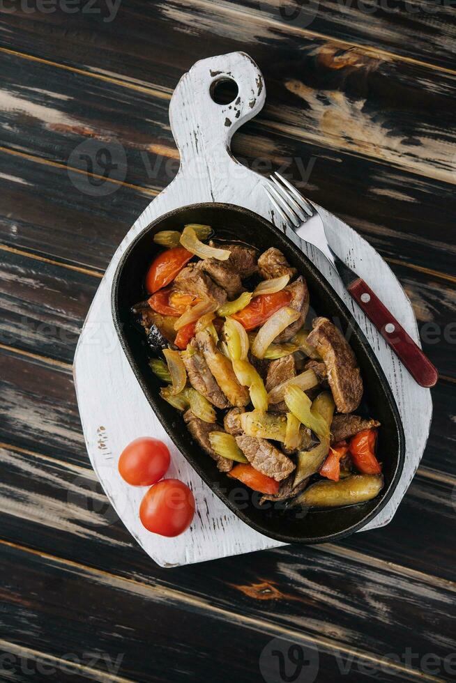 A dish of roasted meat, stewed vegetables on wood photo