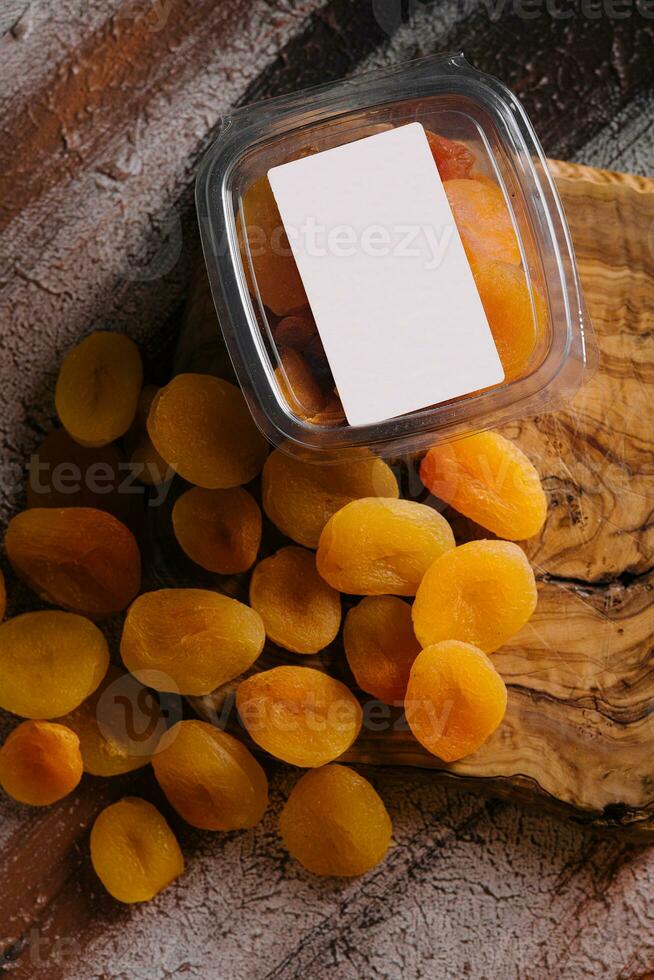 plastic container with dried apricots on wood photo