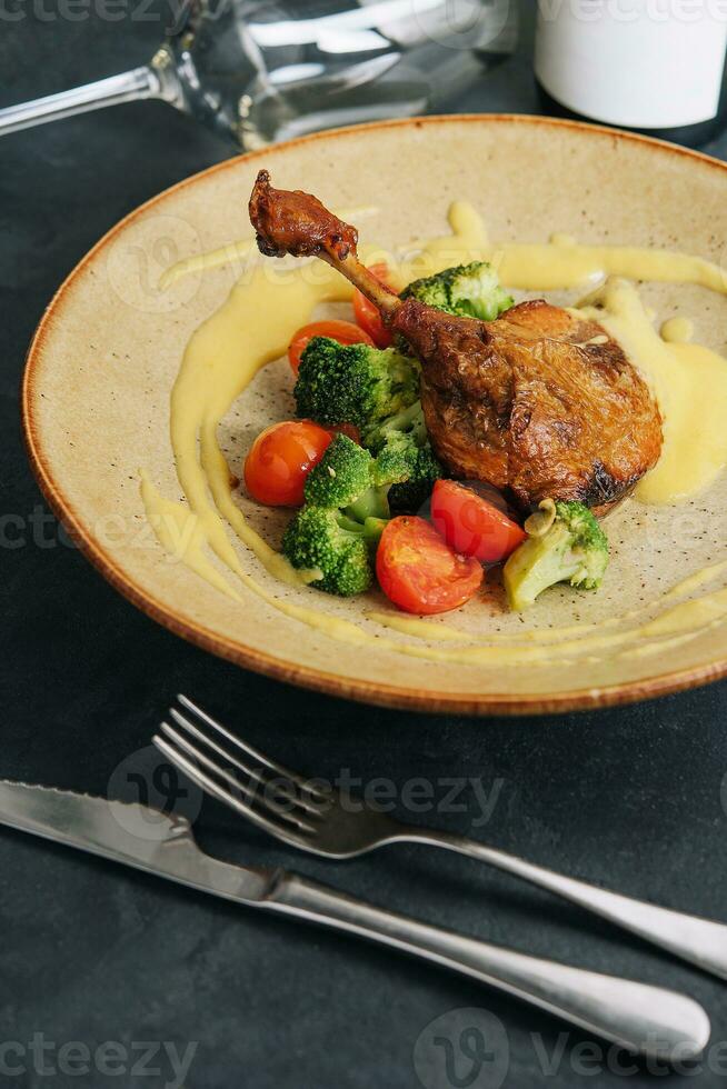 Confit duck leg with broccoli and tomatoes photo
