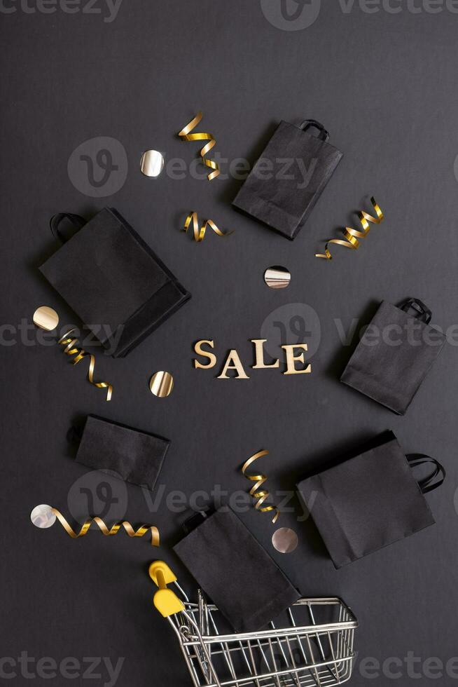 Black friday sale concept. Sale text and shopping bags and shopping cart with festive decorations on black background flat lay, top view. photo