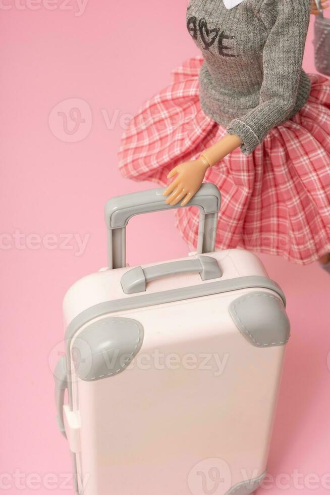 The doll carries a suitcase on wheels. Travel, vacation creative minimalistic concept photo