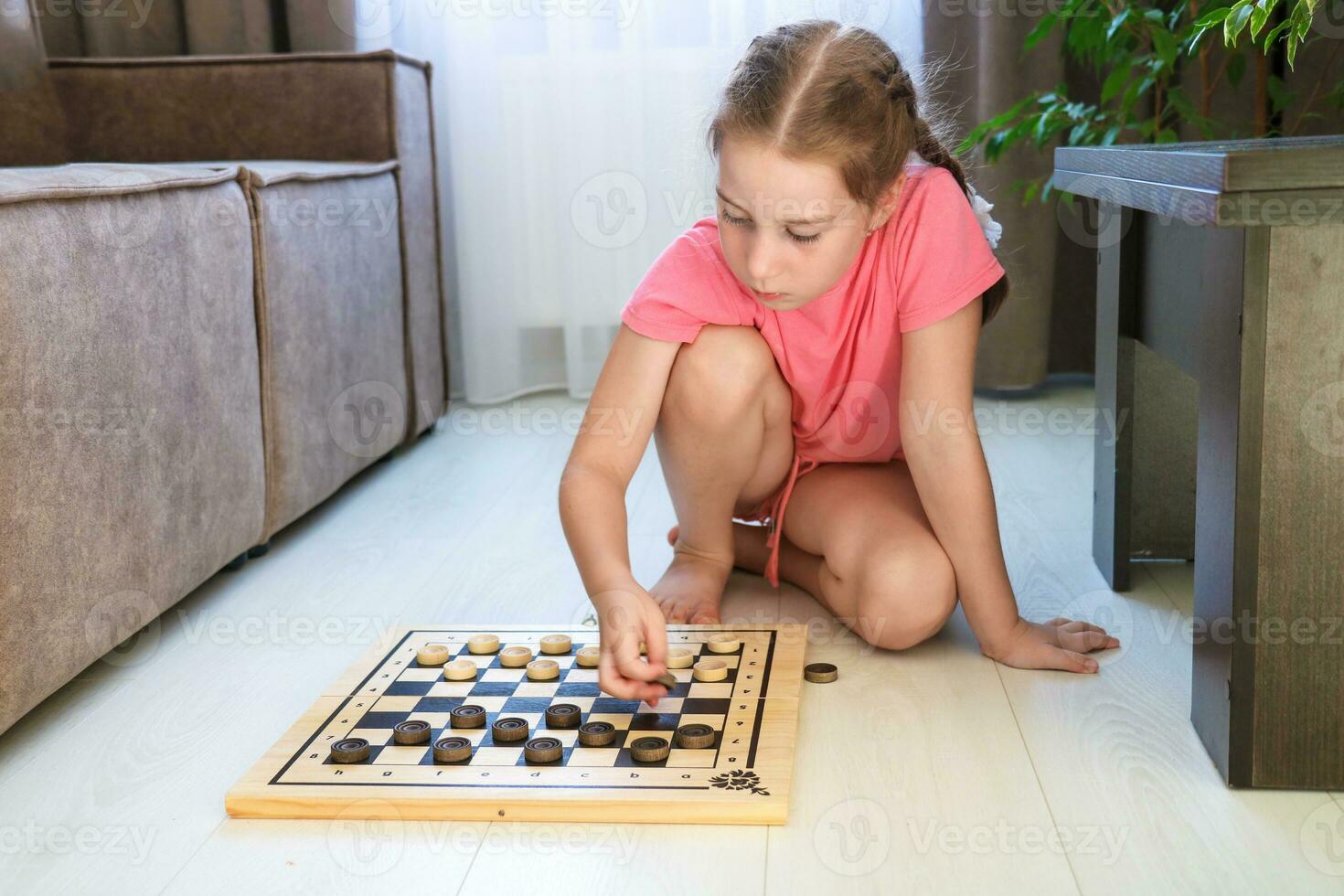 cute girl placing checkers on the board for playing at home on the floor photo