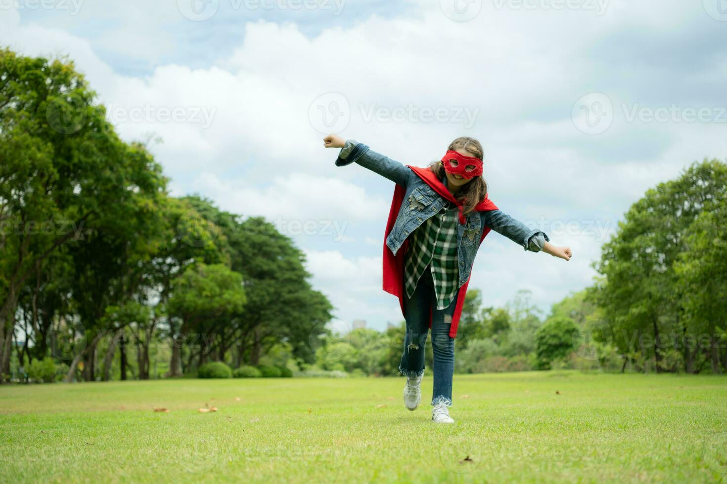 On a beautiful day in the park, a young girl enjoys her vacation. Playful with a red superhero costume and mask. photo