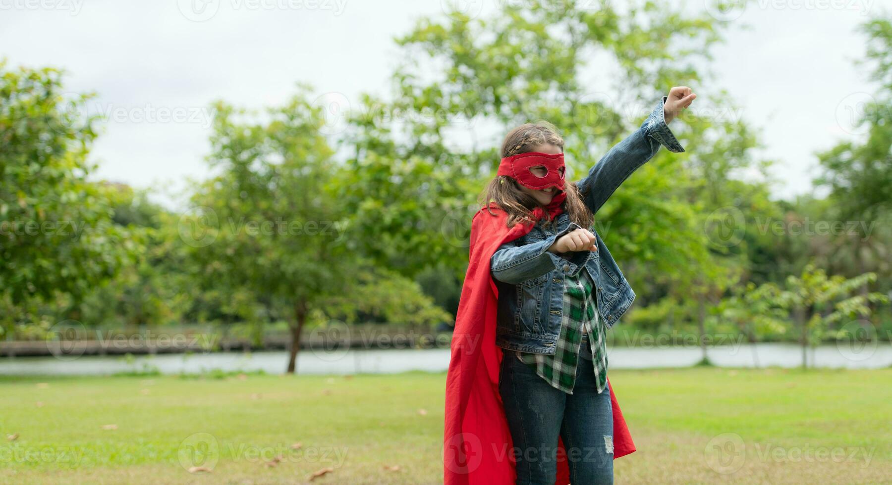 On a beautiful day in the park, a young girl enjoys her vacation. Playful with a red superhero costume and mask. photo