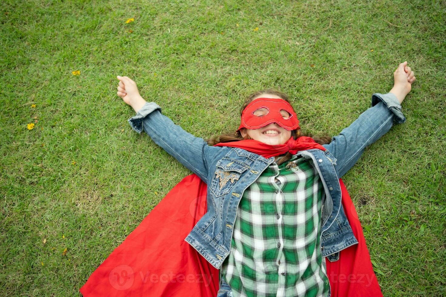 On a beautiful day in the park, a young girl enjoys her vacation. Playful with a red superhero costume and mask. photo