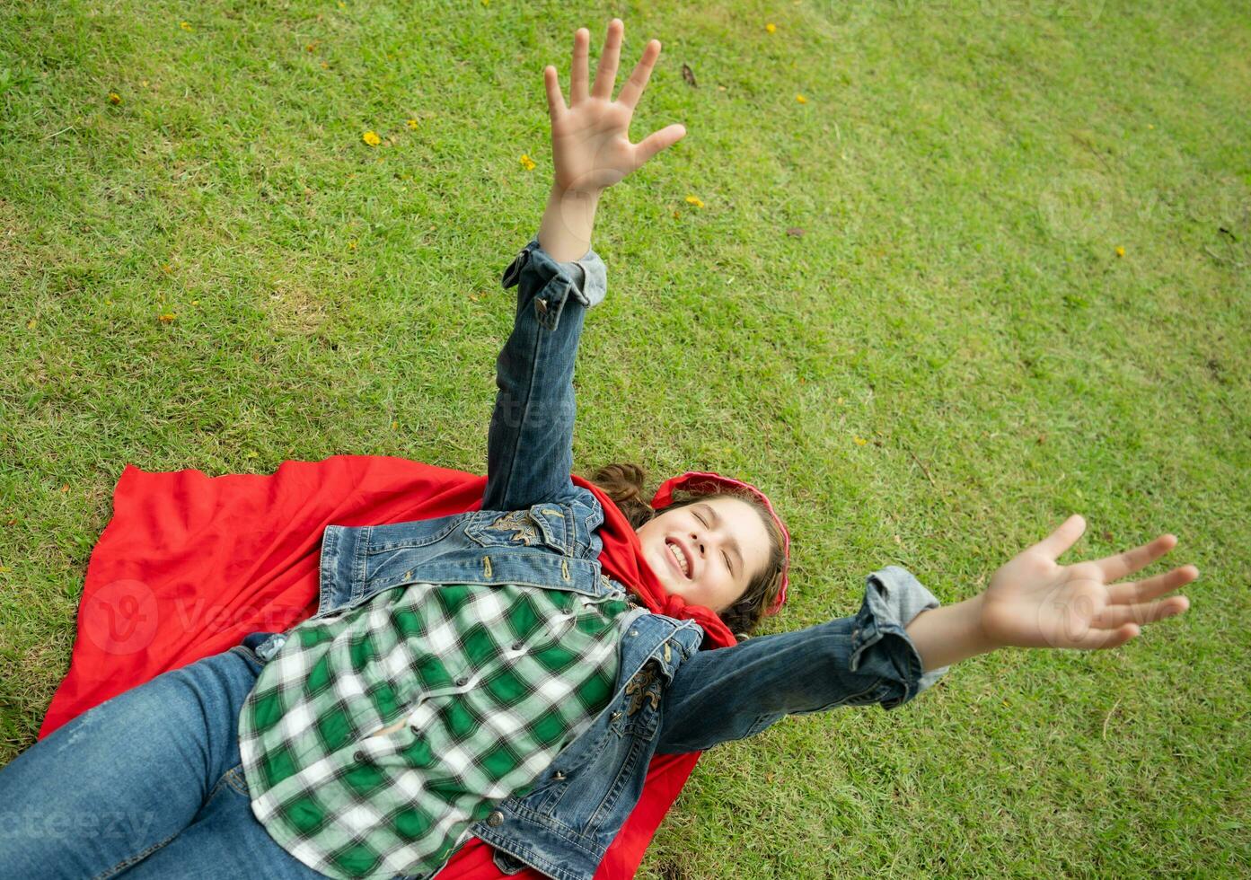 On a beautiful day in the park, a young girl enjoys her vacation. Playful with a red superhero costume and mask. photo
