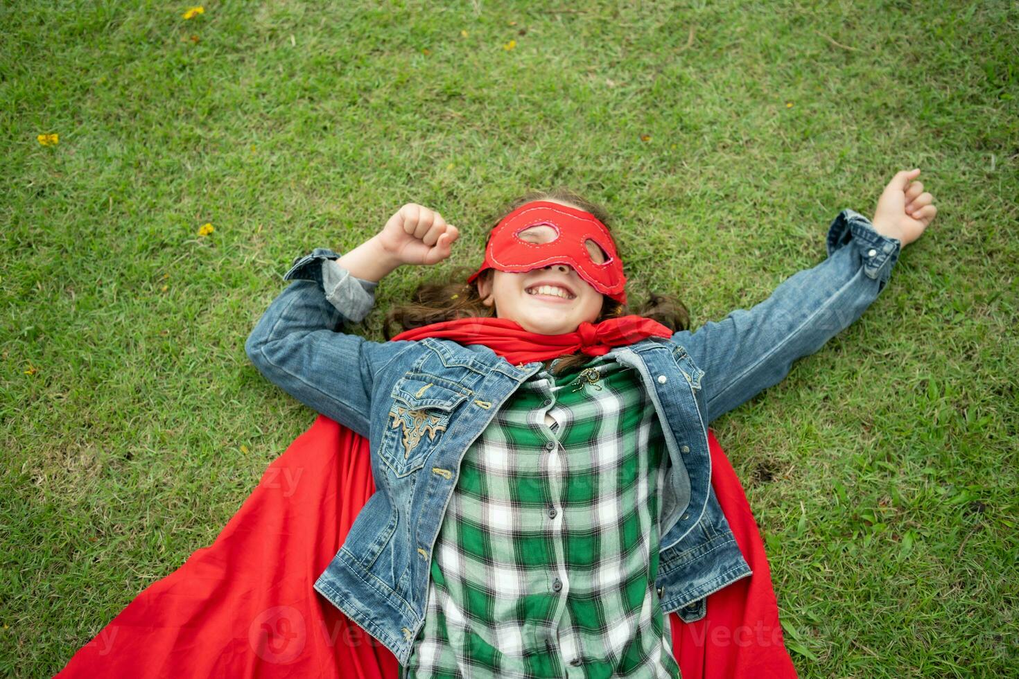 en un hermosa día en el parque, un joven niña disfruta su vacaciones. juguetón con un rojo superhéroe disfraz y mascarilla. foto