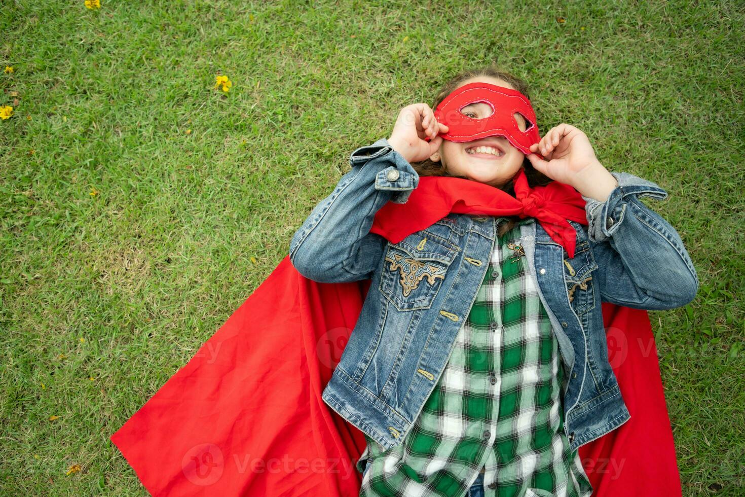 en un hermosa día en el parque, un joven niña disfruta su vacaciones. juguetón con un rojo superhéroe disfraz y mascarilla. foto