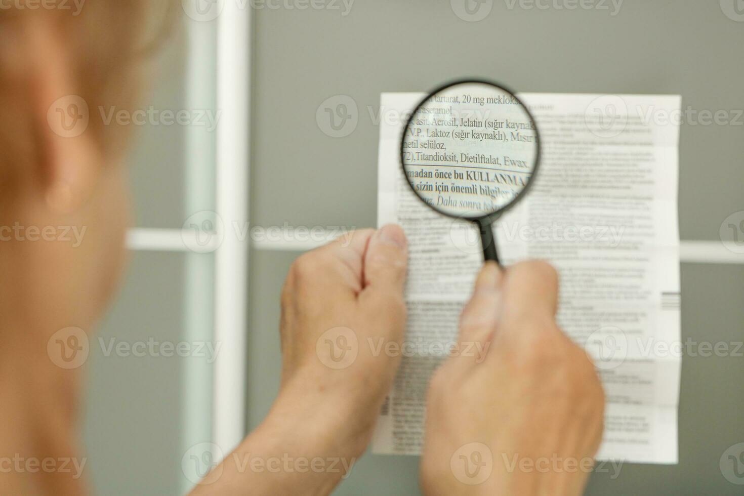 a senior woman reads the instructions for medicine in Turkish through a magnifying glass photo