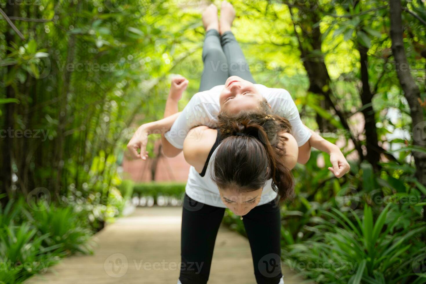 Young female and little girl disciple in the garden there are wooden walkways and a tunnel of fresh green trees. with yoga activities for health photo