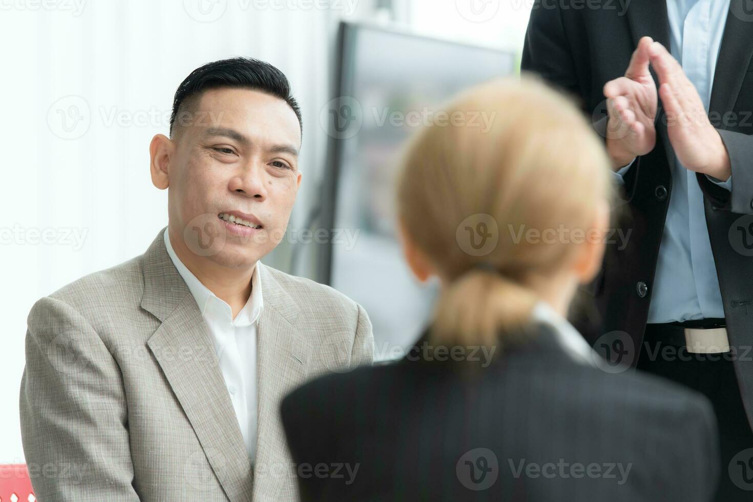 Confident Asian businessman sitting at chair and talking with his colleague in office photo