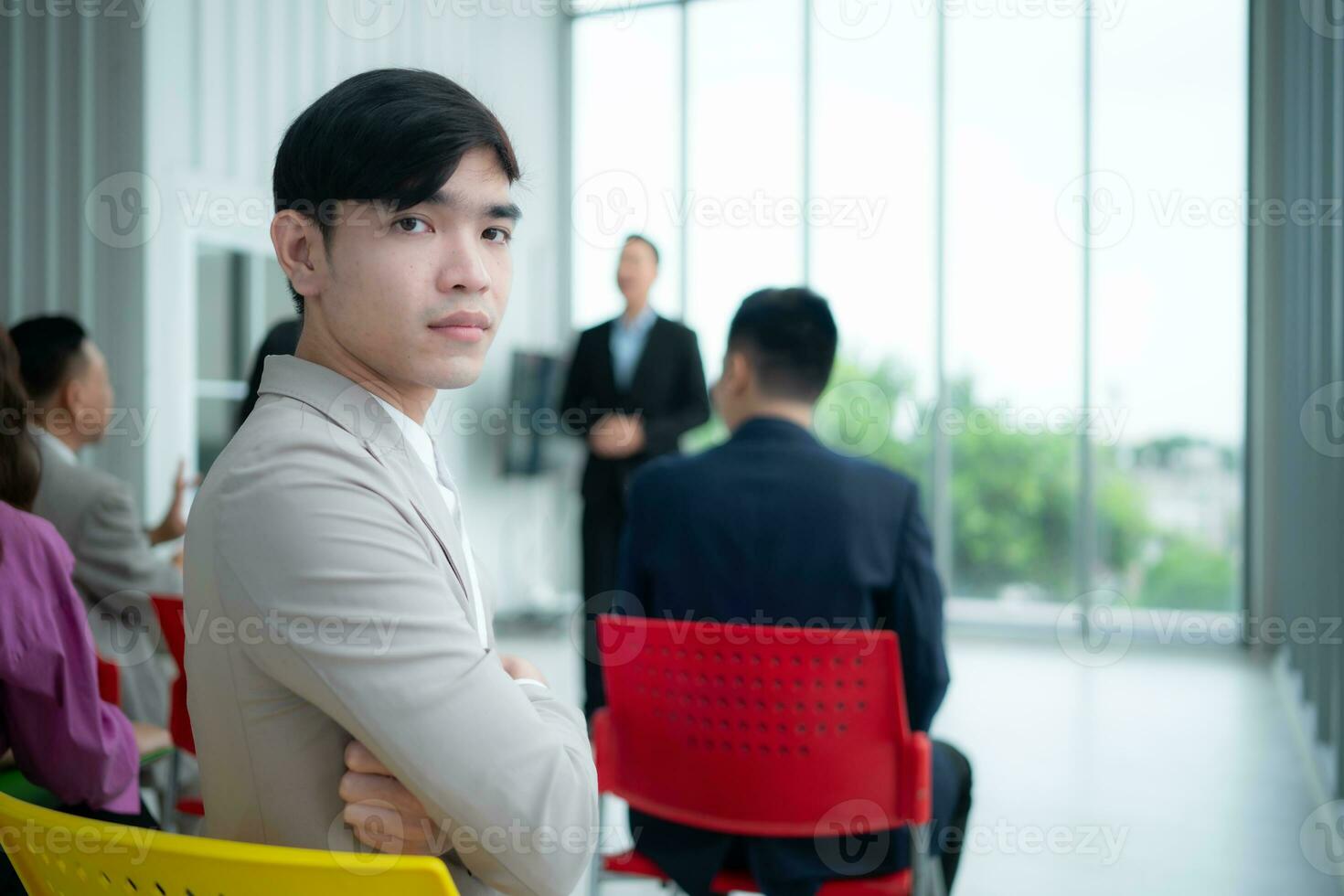 Portrait of a young Asian businessman sitting behind a seminar room with a colleague in the foreground listening to the lecture photo