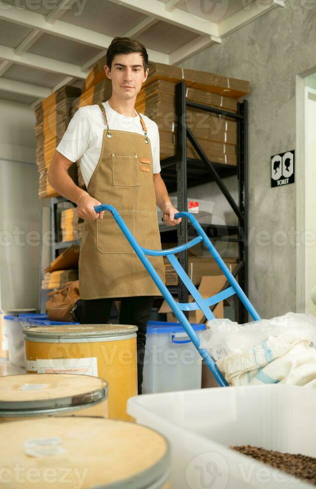 Worker in apron standing with trolley in the coffee beans warehouse photo