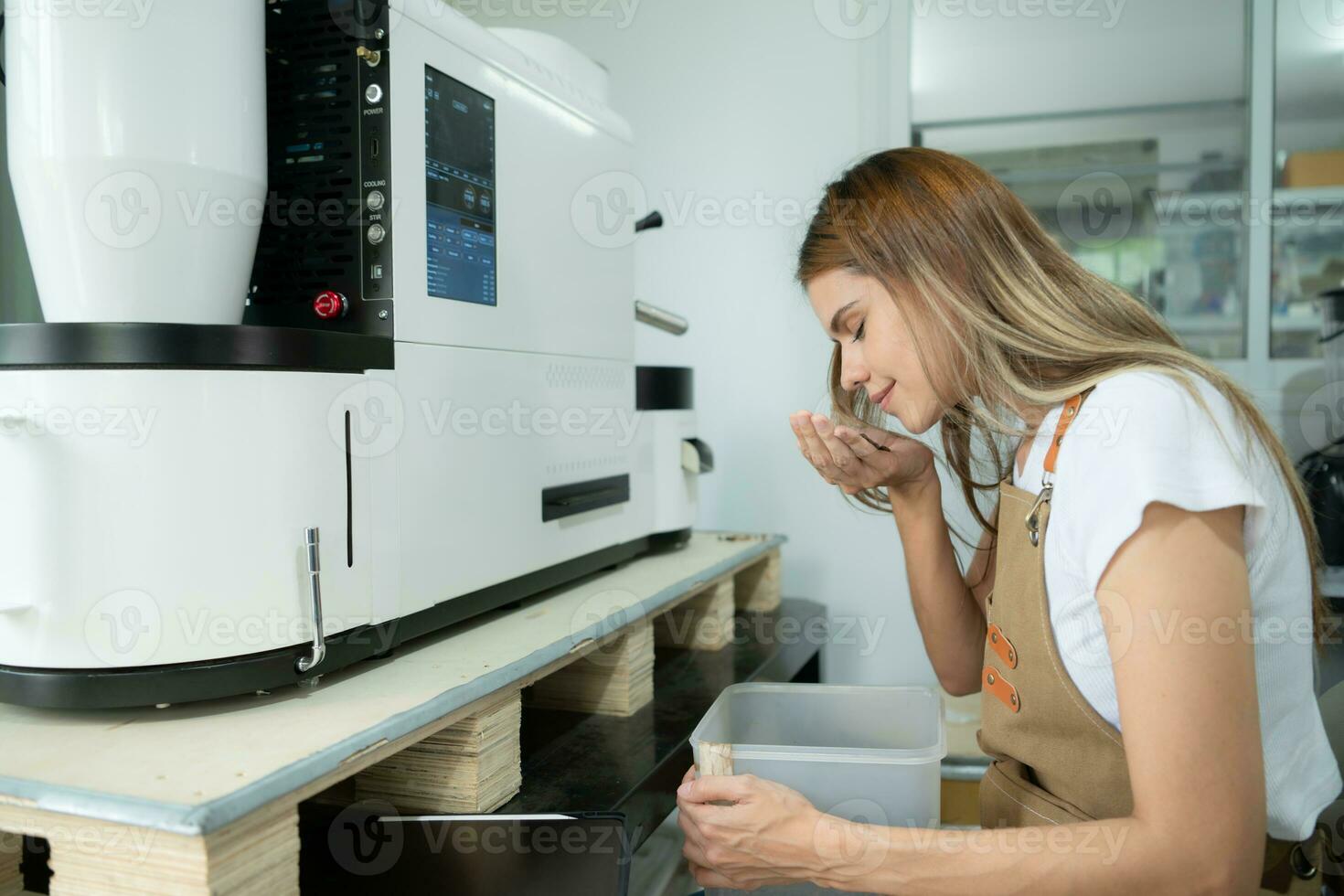 Young woman in apron using digital tablet for checking quality of of coffee beans with digital roaster photo