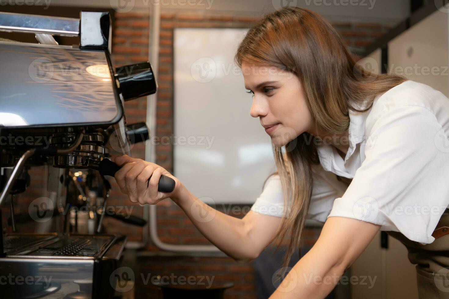 Young female barista preparing coffee in cafe. Female barista using coffee machine. photo