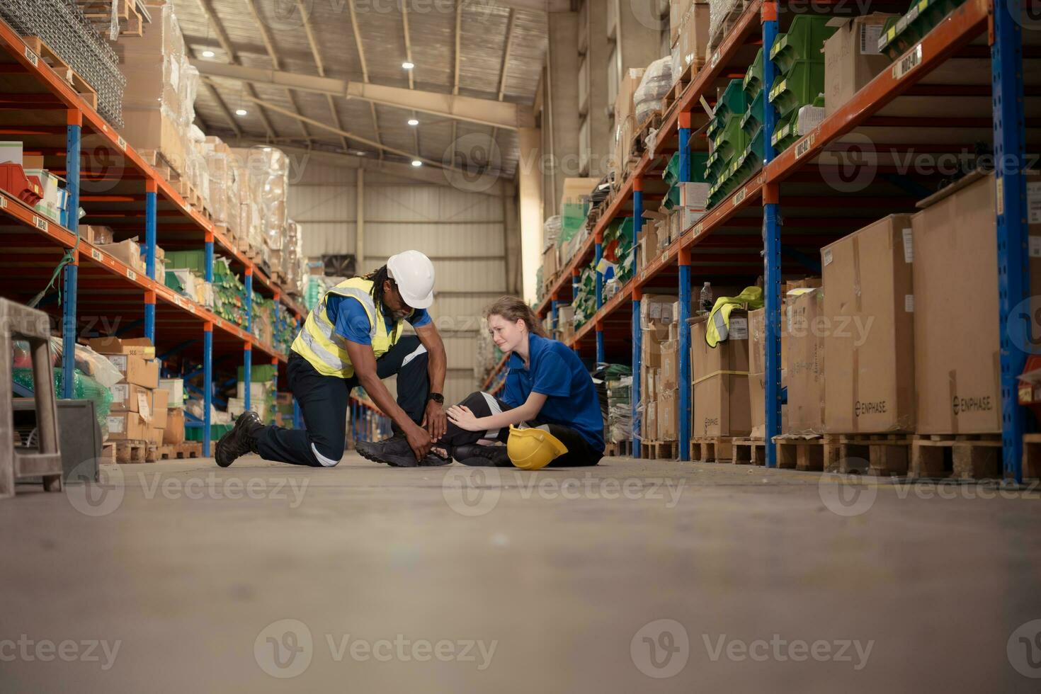 A warehouse worker consoles and helps a female worker who cries out in pain after a leg accident in a large warehouse photo