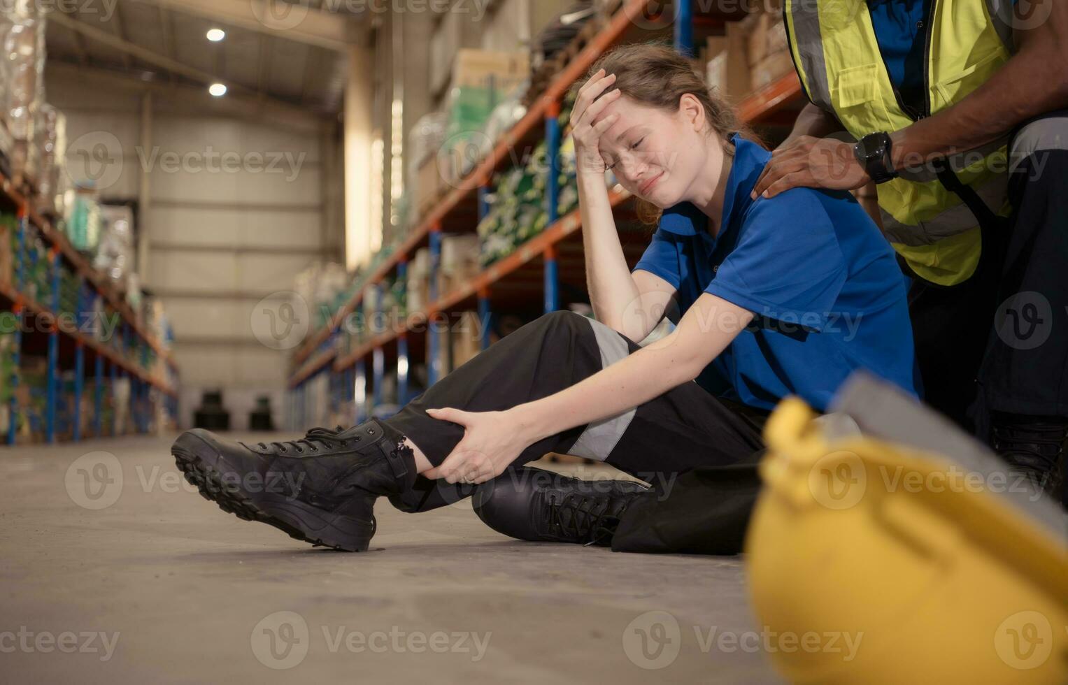 A warehouse worker consoles and helps a female worker who cries out in pain after a leg accident in a large warehouse photo