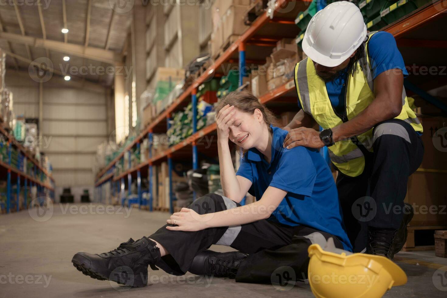 A warehouse worker consoles and helps a female worker who cries out in pain after a leg accident in a large warehouse photo