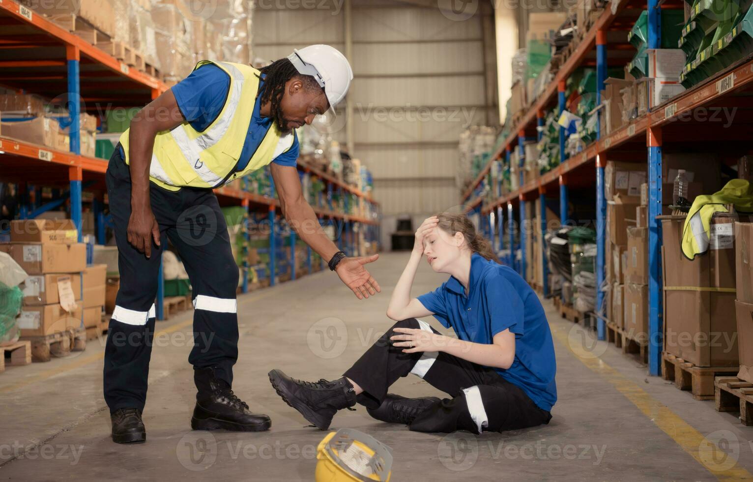 A warehouse worker consoles and helps a female worker who cries out in pain after a leg accident in a large warehouse photo