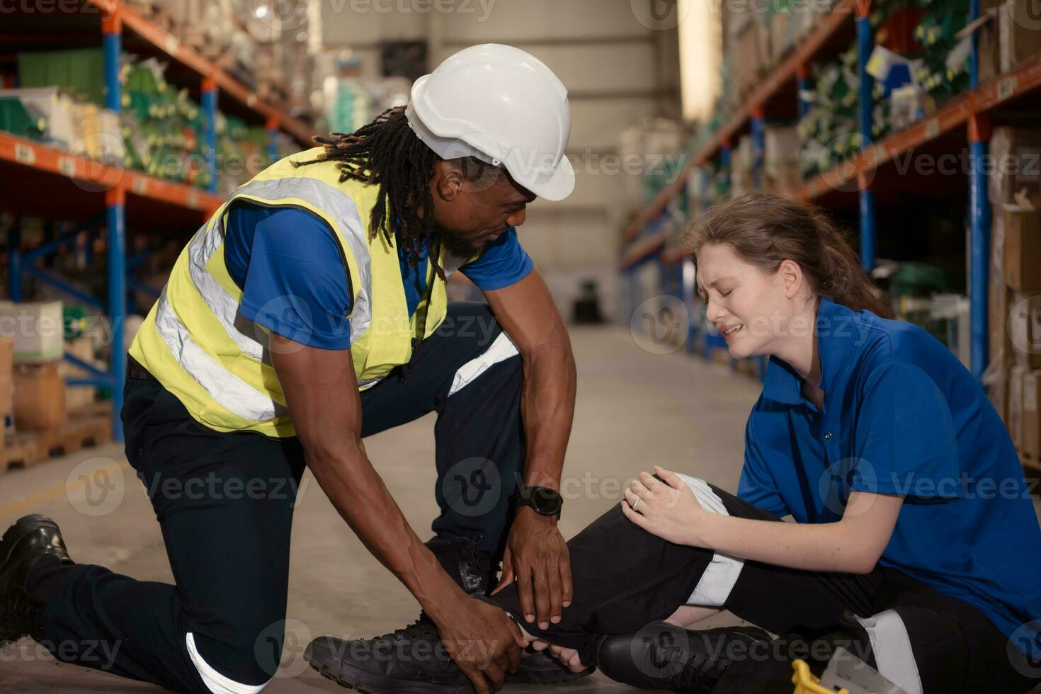 A warehouse worker consoles and helps a female worker who cries out in pain after a leg accident in a large warehouse photo