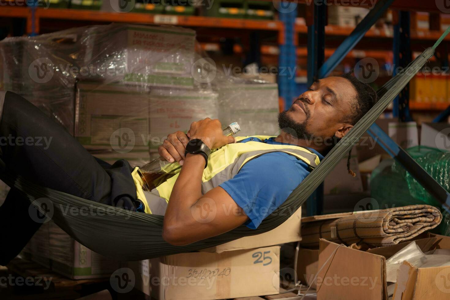 Portrait of young male worker relaxing in hammock with alcohol bottle in warehouse photo