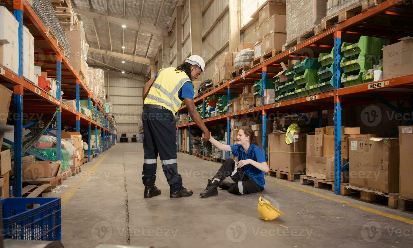 A warehouse worker consoles and helps a female worker who cries out in pain after a leg accident in a large warehouse photo