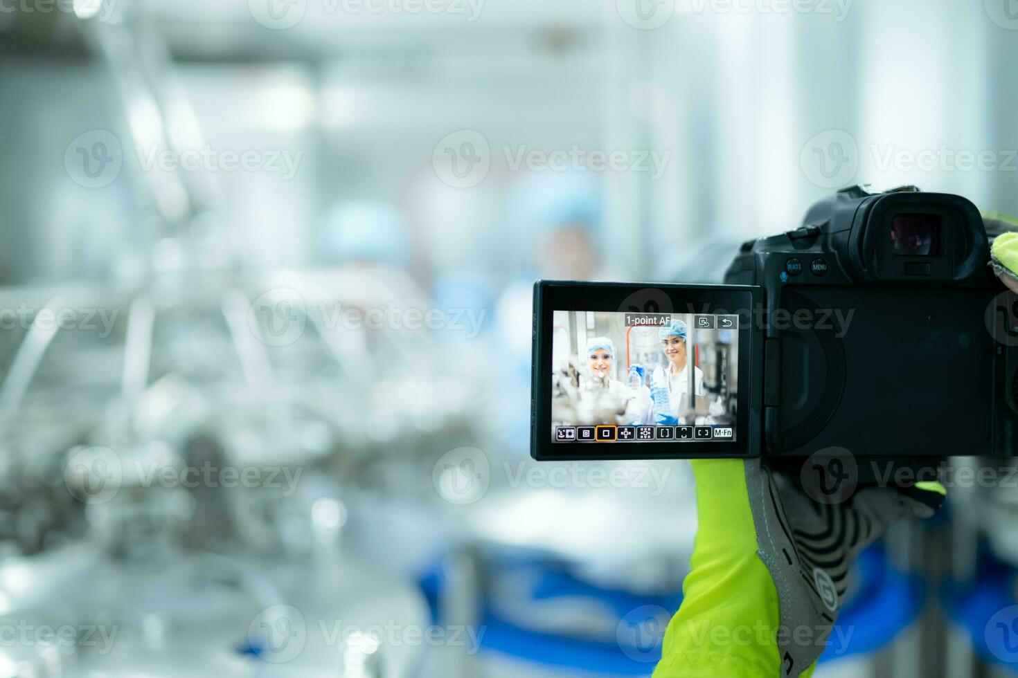 A photographer holding a digital camera on a production line is recording the work of a production line worker. To be used for public relations and further marketing photo