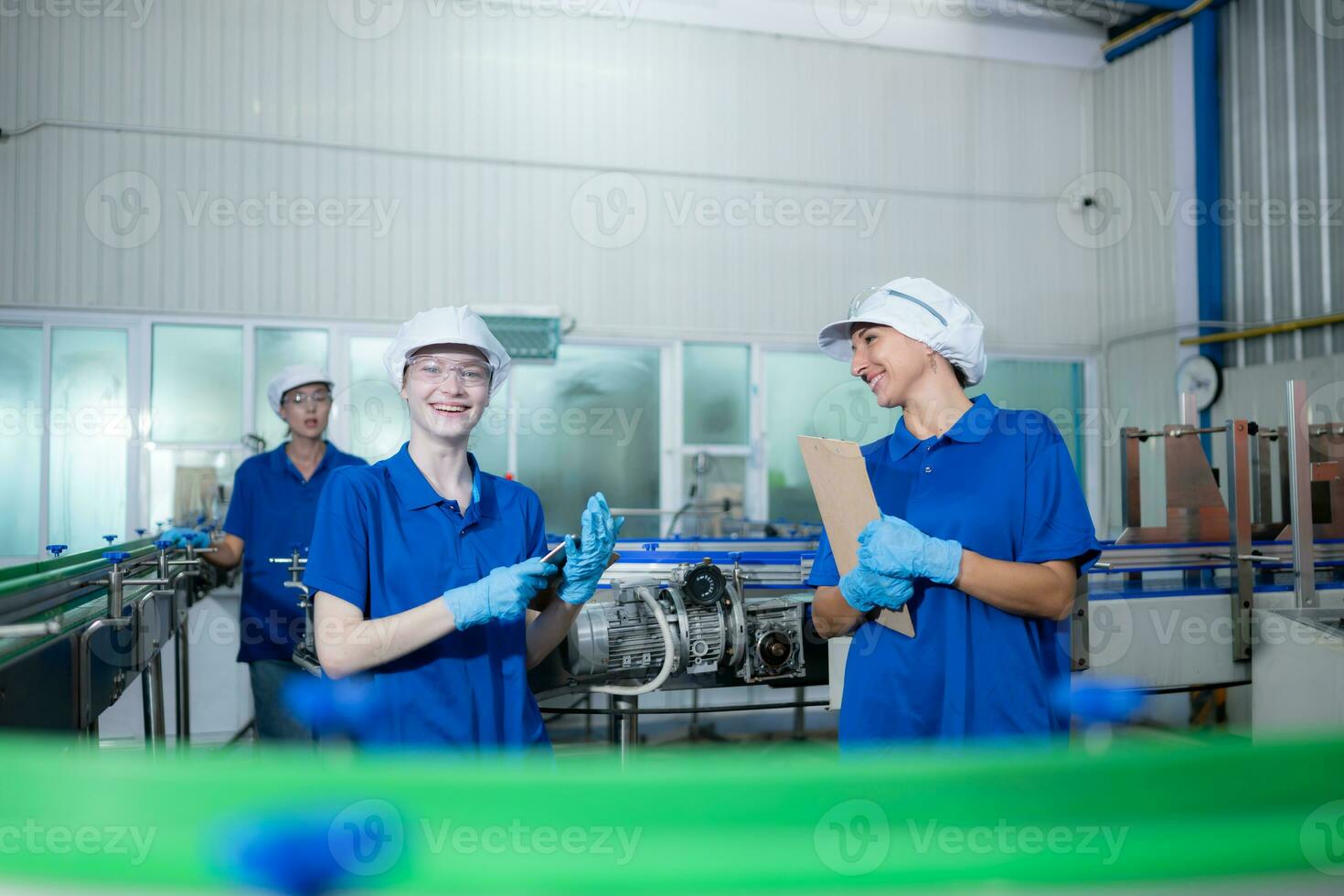 joven mujer fábrica trabajadores en azul uniformes y sombreros trabajando juntos en Bebiendo agua fábrica foto