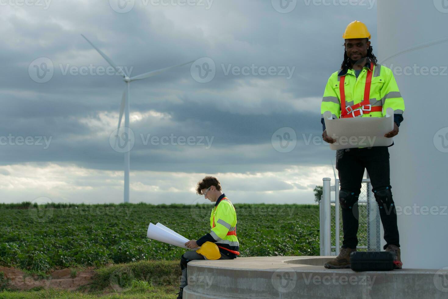 Engineers and technicians work together on the tower base of a large wind turbine with a wind turbine field in the background, The concept of natural energy from wind. photo