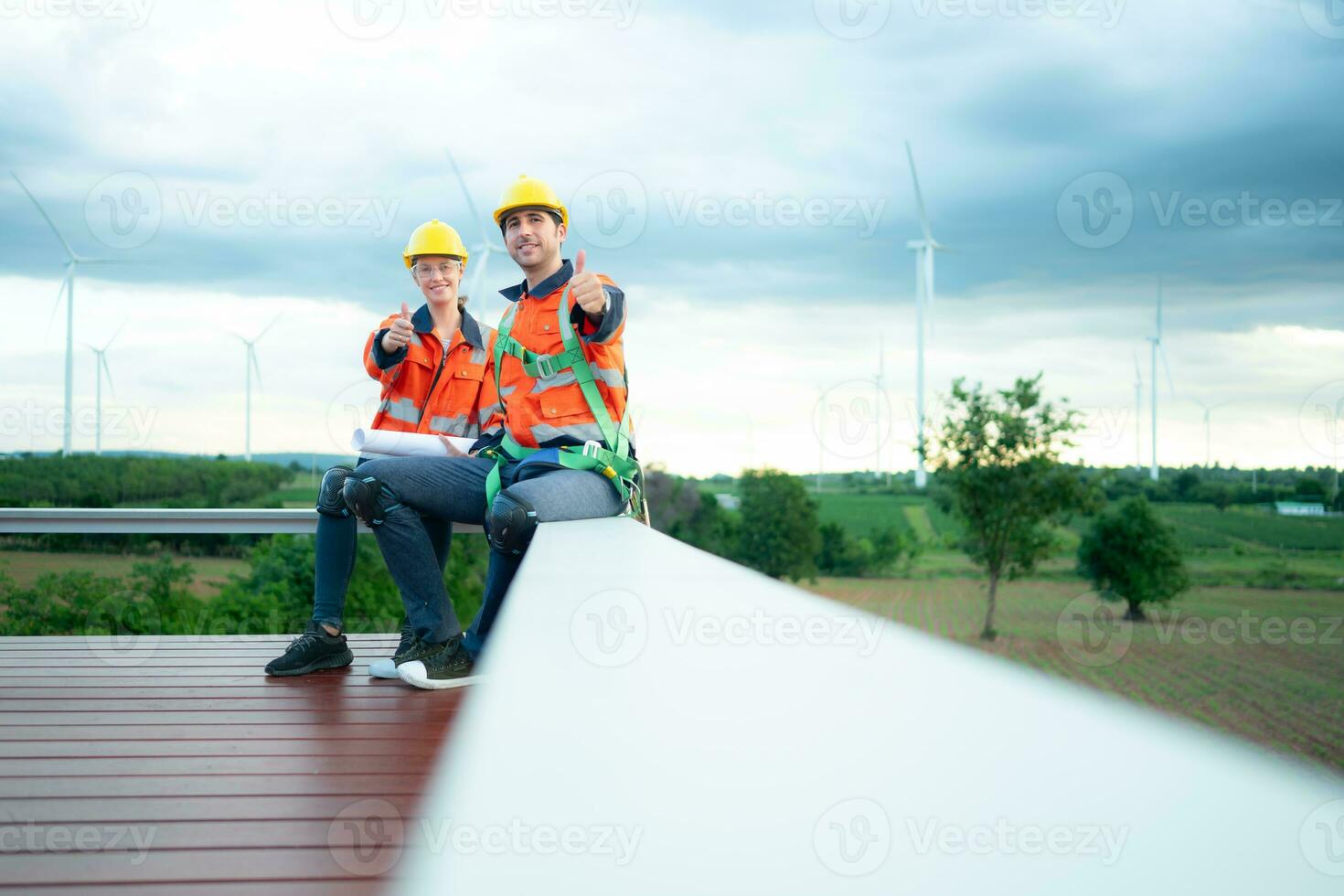 Two engineers discussing a project of wind turbine, They are sitting on a wooden platform, The concept of natural energy from wind. photo
