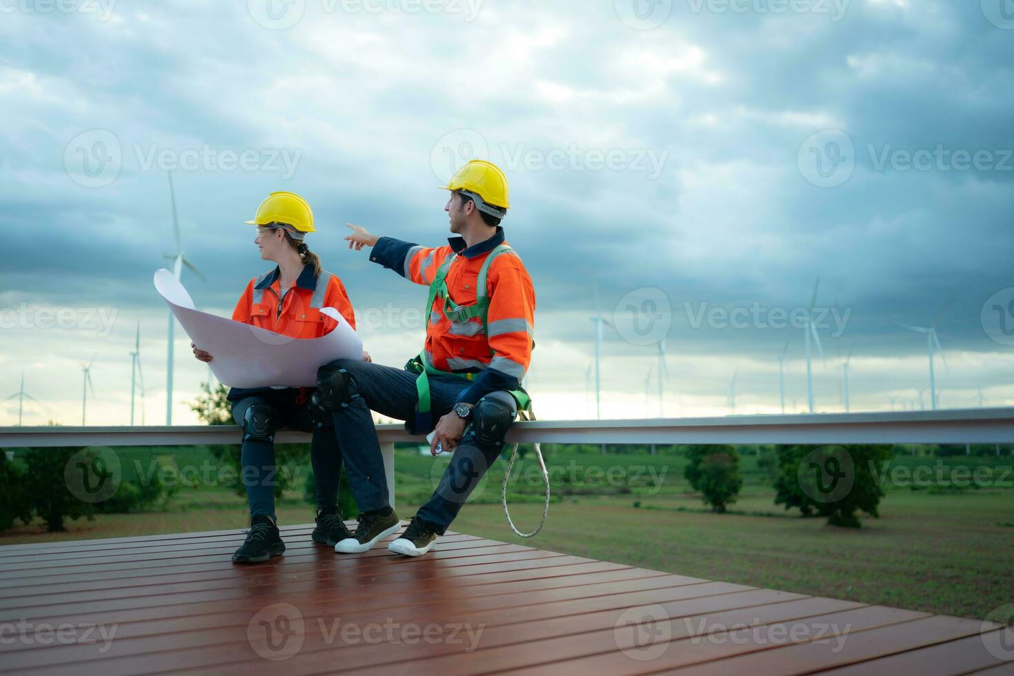 Engineer and technician discussing blueprint on the building site with wind turbine background photo