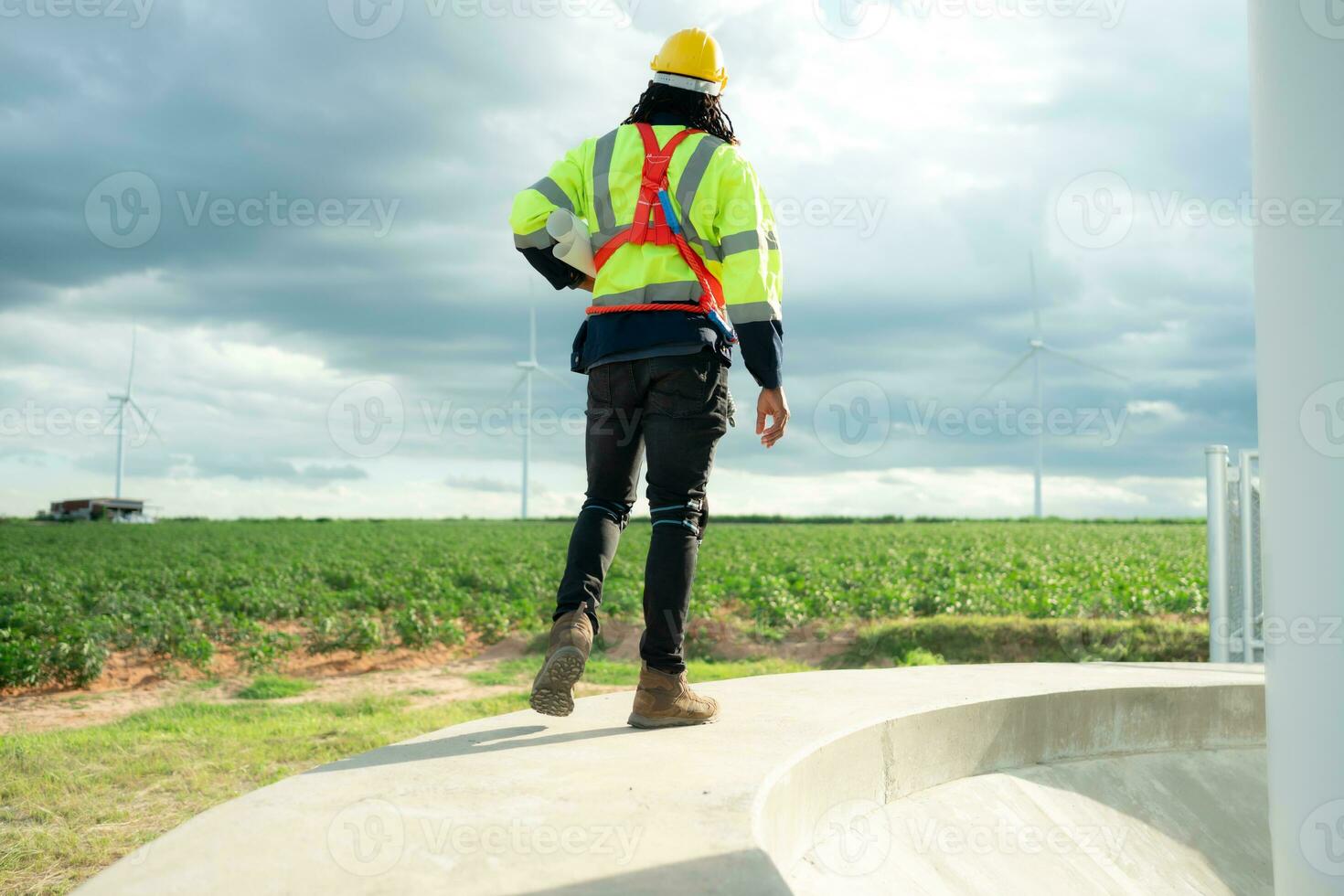 posterior ver de ingeniero con la seguridad casco y reflexivo chaleco caminando en viento turbina campo foto