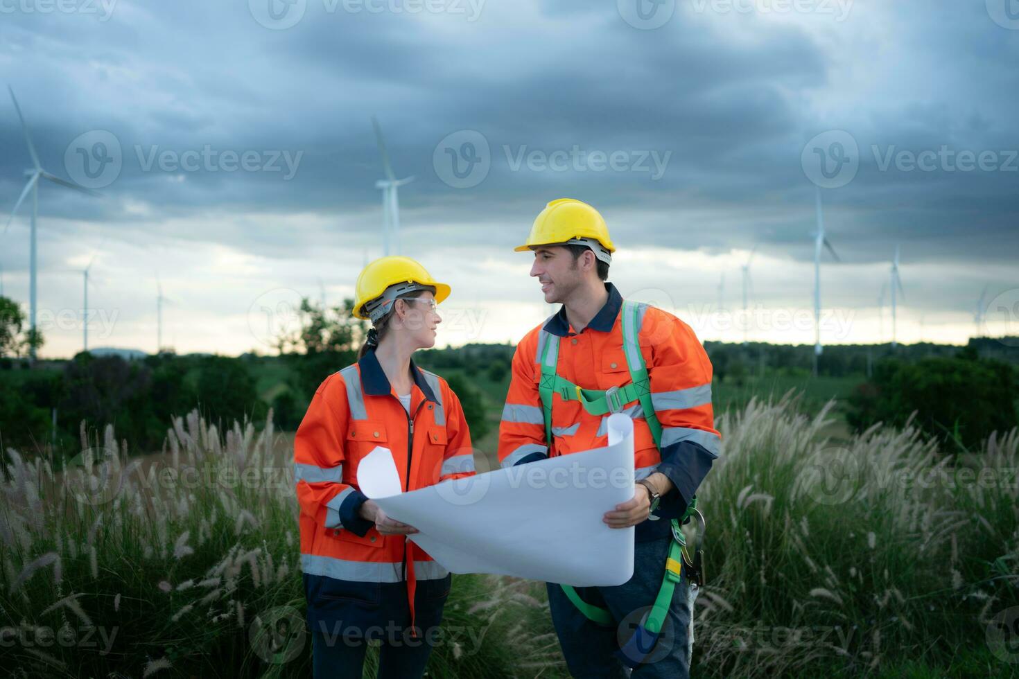 dos ingenieros trabajando en un construcción sitio con viento turbinas en el antecedentes foto