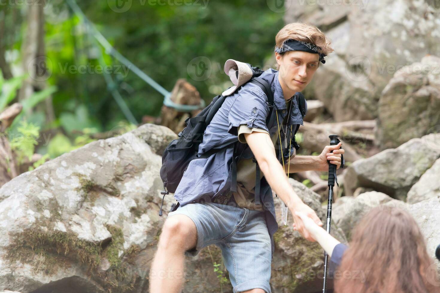 Young couple hiking in forest help each other in the climbing, Man and woman trekking in nature. photo