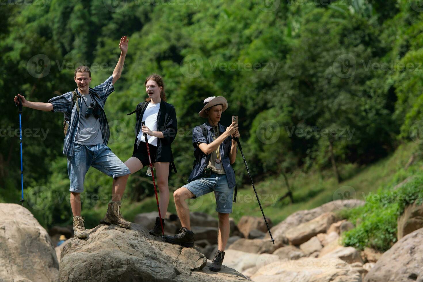 Young man hiker with backpack and trekking poles with a young man helping to pull him up to stand on the rock photo
