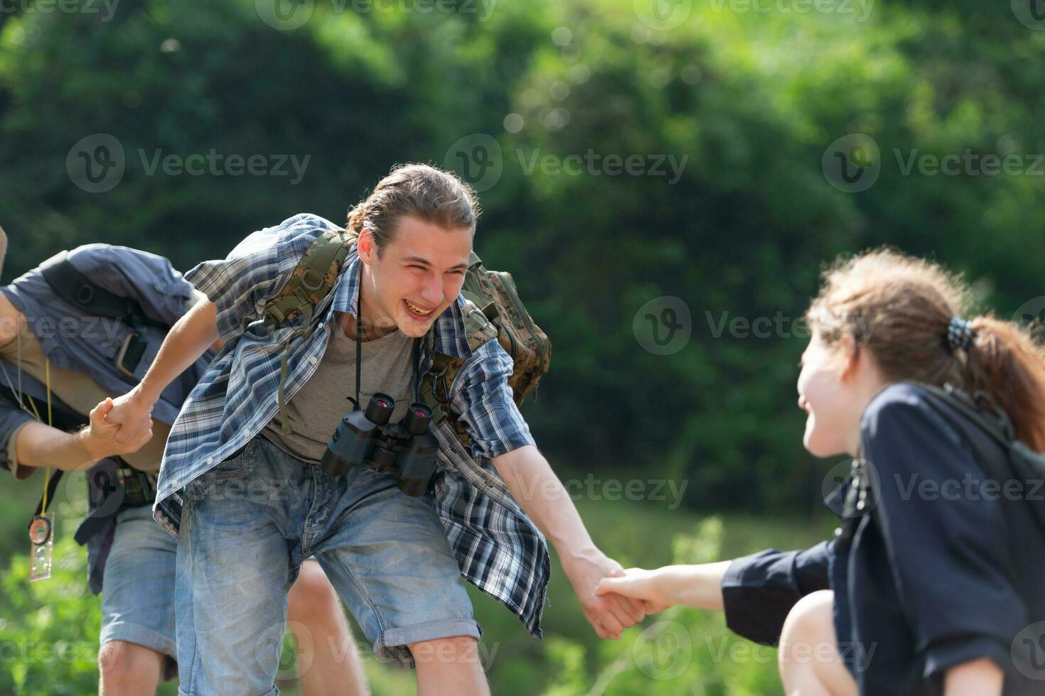 Group of friend on a sunny day in the forest Young group hiker with backpack and trekking poles helping to pull each other up to stand on the log photo
