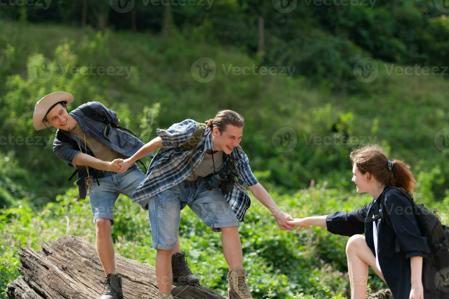 Group of friend on a sunny day in the forest Young group hiker with backpack and trekking poles helping to pull each other up to stand on the log photo