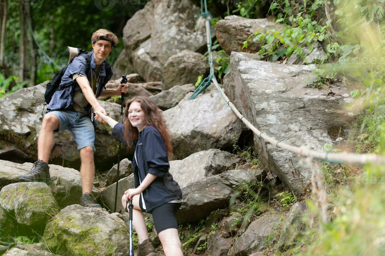 Young couple hiking in forest help each other in the climbing, Man and woman trekking in nature. photo