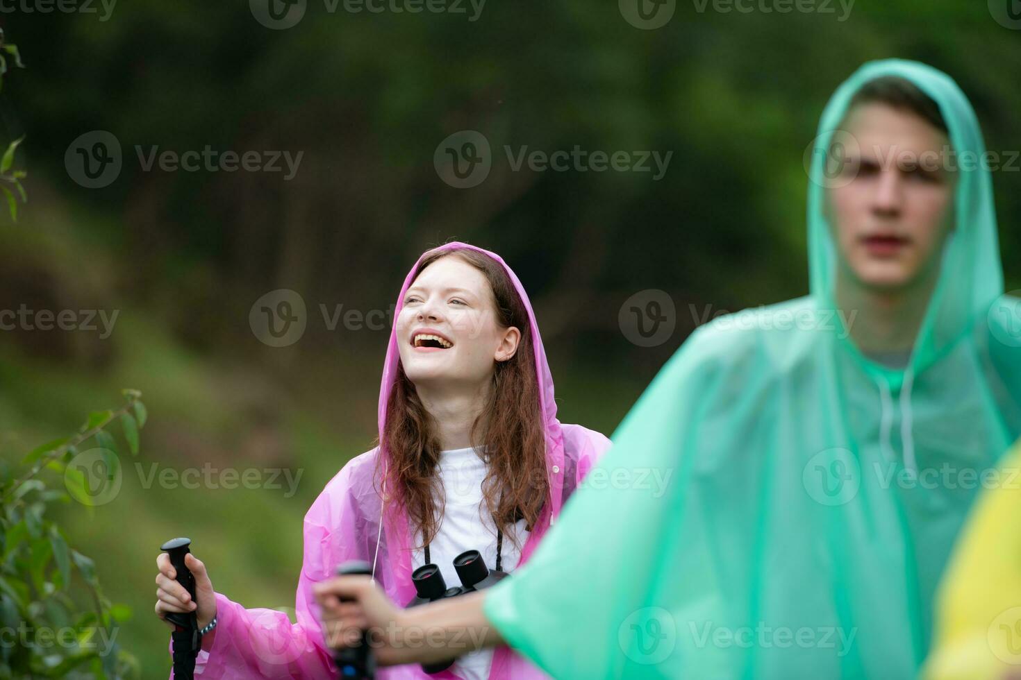 Group of friends in raincoats walking on the forest path, Hiking concept. photo