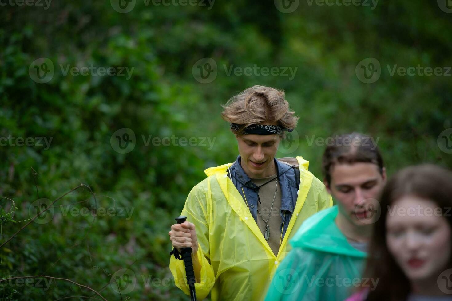 Group of friends in raincoats walking on the forest path, Hiking concept. photo