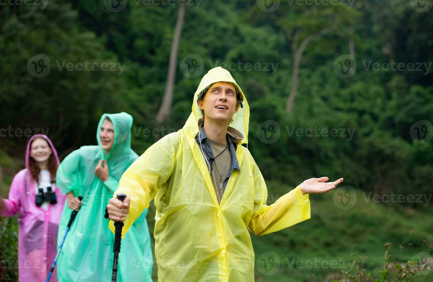 Group of friends in raincoats walking on the forest path, Hiking concept. photo