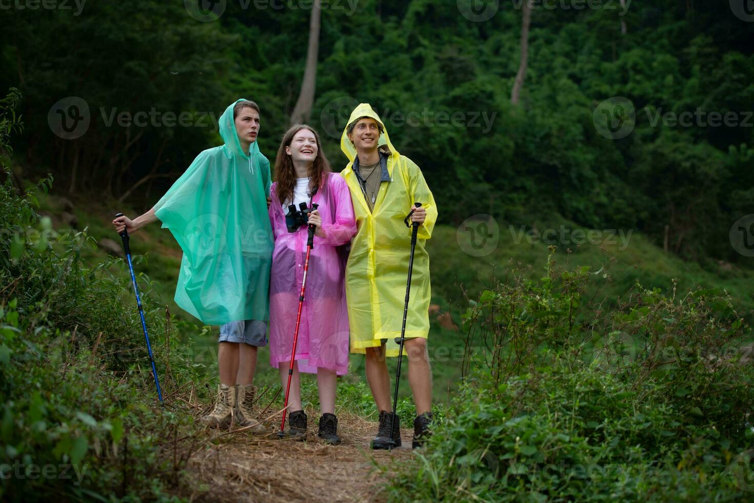 Group of happy friends in raincoats and raincoats looking at mountain and forest after the rain stoped photo