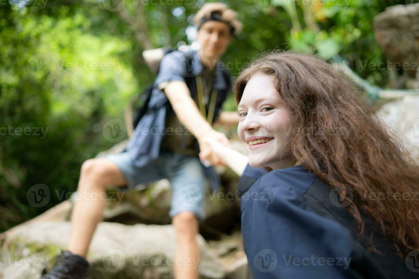 Young couple hiking in forest help each other in the climbing, Man and woman trekking in nature. photo