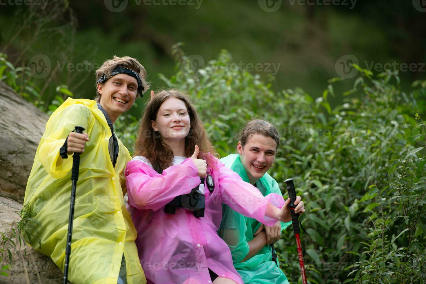 Group of friends in raincoats with backpacks on a hike in the forest, Prepare to hiking after the rain has stopped. photo