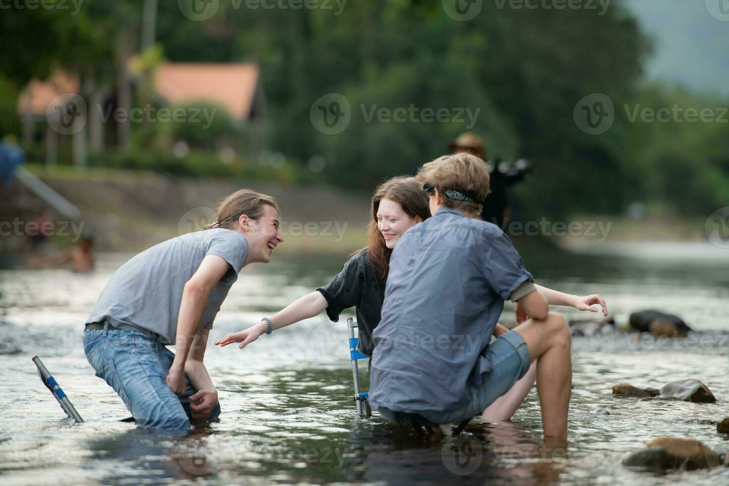 Group of friends are talking and having fun in the middle of the river flowing in front of the campsite. photo